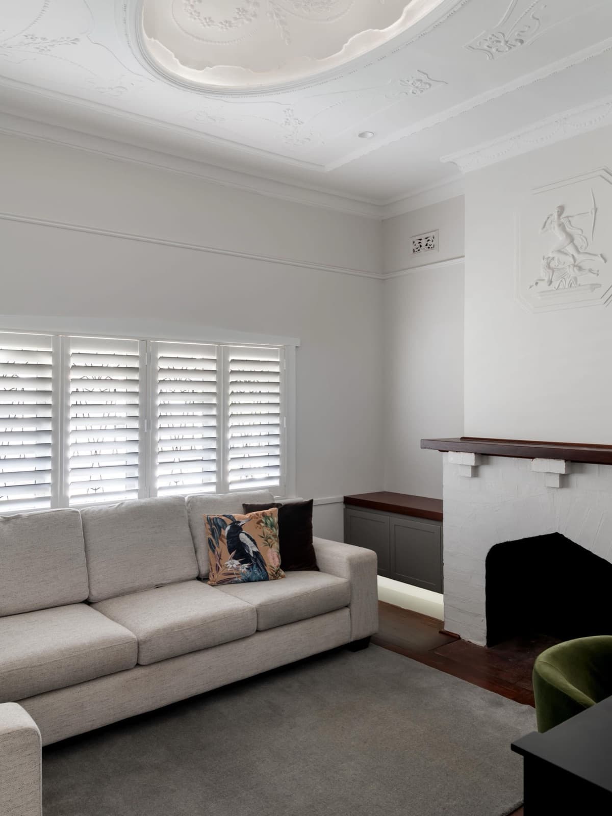 Heritage lounge with a painted ornate ceiling rose and cornices, and a timber mantel over a painted brick fireplace